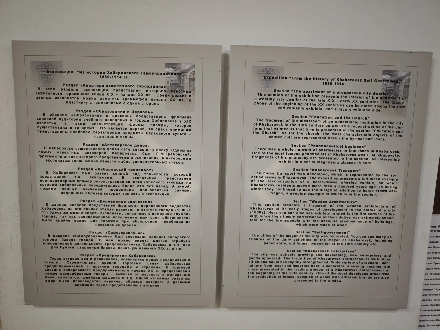 Two information boards in Russian and English introduce the exhibition content. The left board provides detailed descriptions of each exhibition section, while the right board offers English translations to assist international visitors. The background of the boards is light gray, and the text is clearly legible.