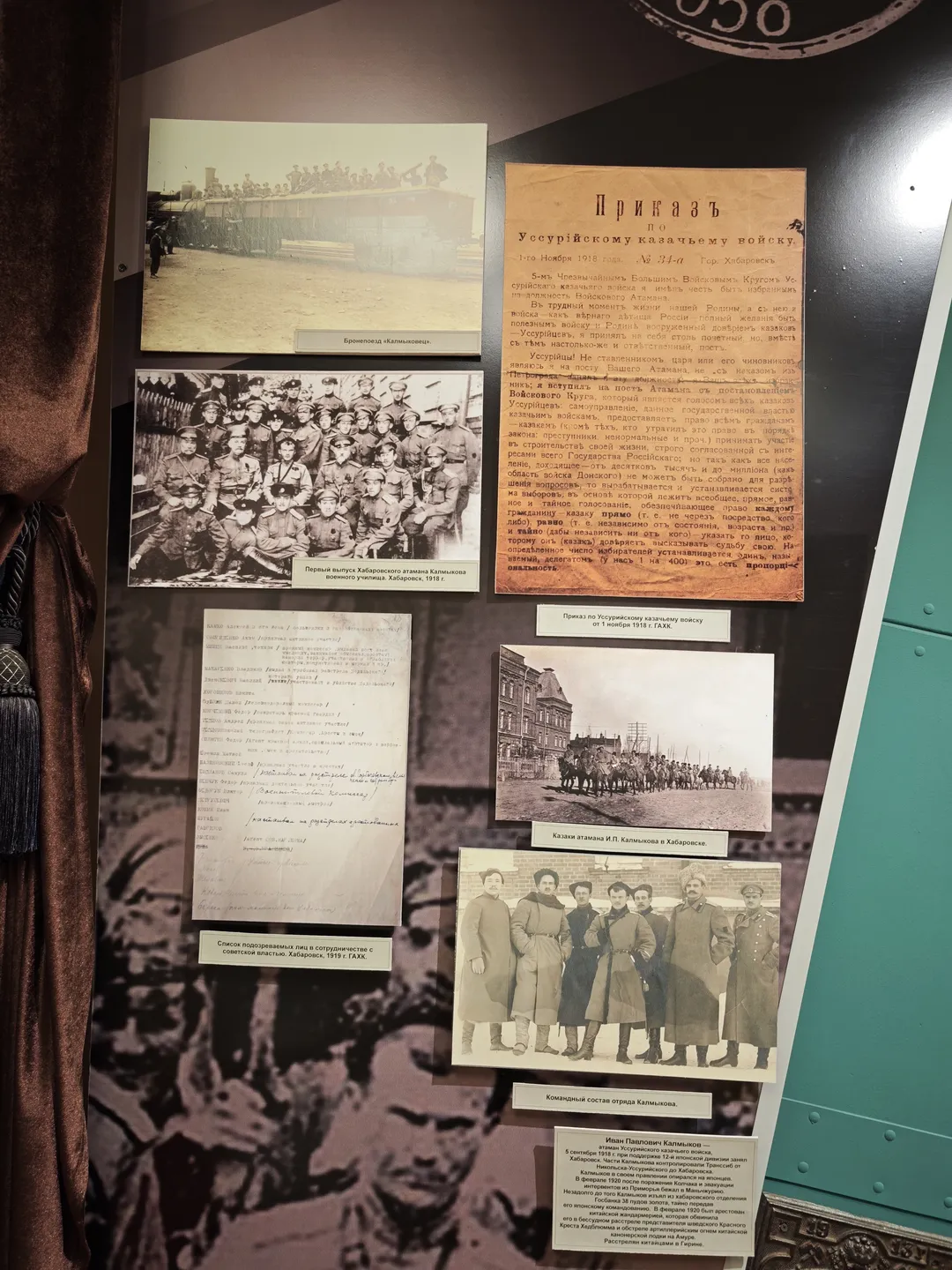Several historical photographs and documents are hung on the wall, including a group photo of soldiers and military orders. Labels are placed beneath the photos, set against a dark wall.