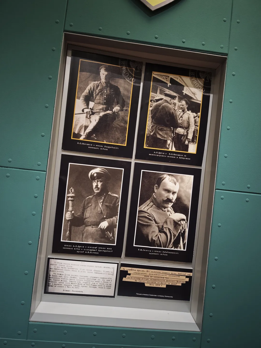 Four black-and-white portrait photographs are embedded into a green wall, with explanatory texts underneath. The individuals in the photos are dressed in military uniforms, each posing differently.