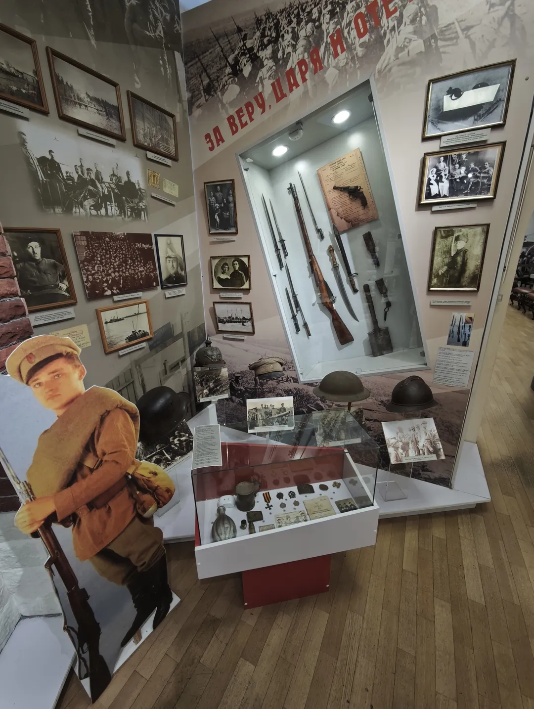 The exhibition room showcases weapons, helmets, and historical photos. Multiple black-and-white photos are hung on the walls, with a glass display case at the center.