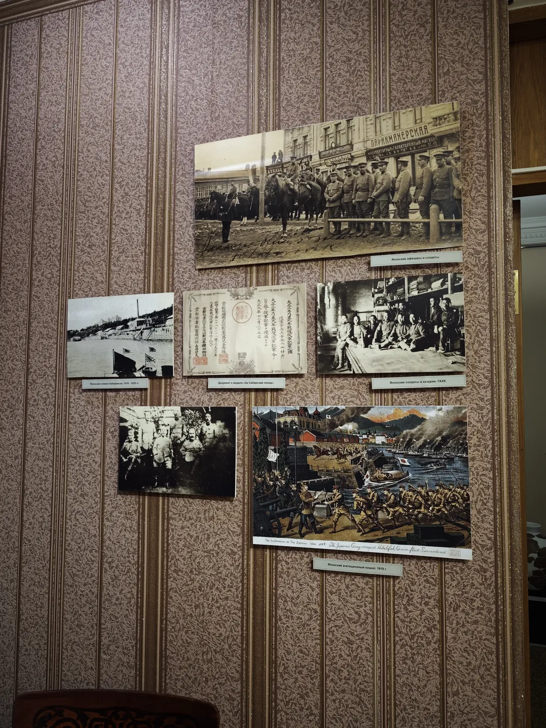 The wall displays several historical photographs, along with a colorful painting depicting a war scene. The photos depict soldiers in various activities and environments.