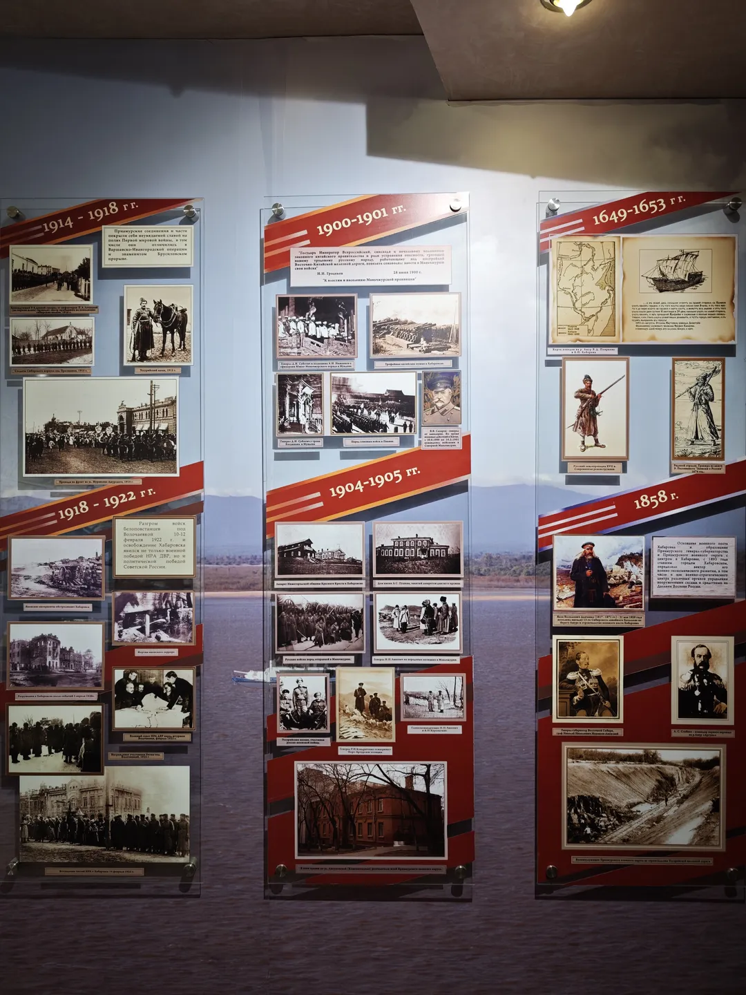 Three exhibition boards display historical photographs and information from different years: 1914-1918, 1900-1901, and 1649-1653. Each board contains multiple black-and-white photos and corresponding descriptions. The background of the boards is red and white.