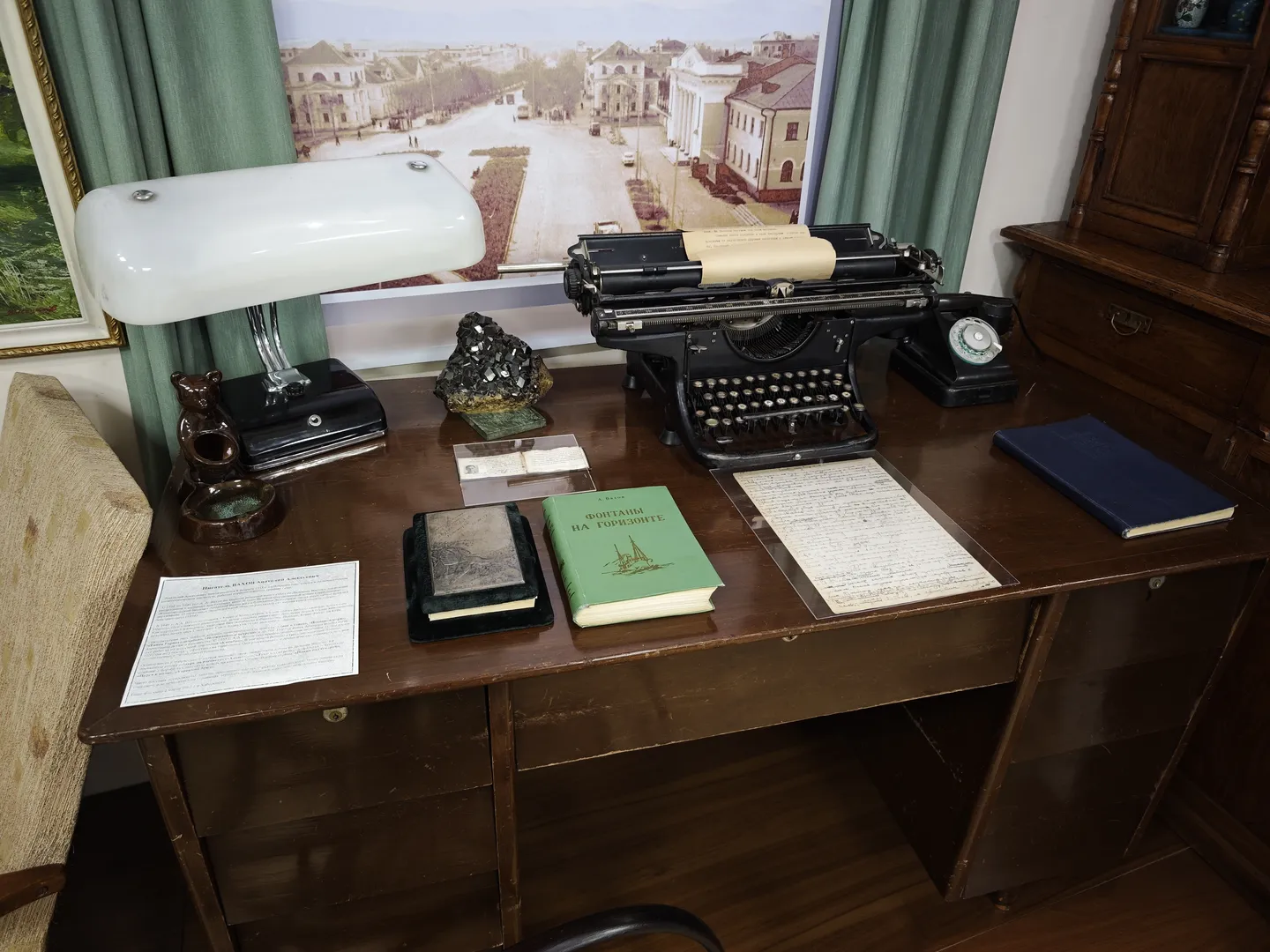 A wooden desk with a typewriter, a book, and several documents. The desk also has a desk lamp and a small globe.