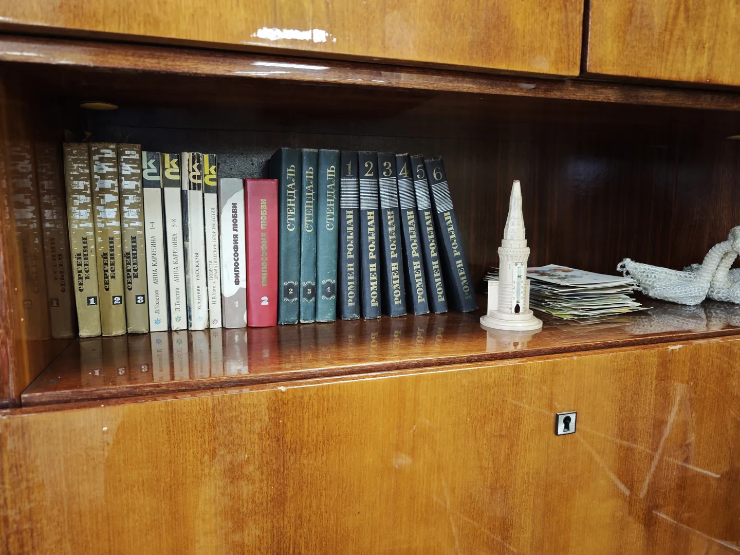 A bookshelf neatly arranged with books of various cover colors. To the right of the shelf, there is a small tower-like decorative item and a stack of paper. The surface of the shelf is smooth, reflecting light.