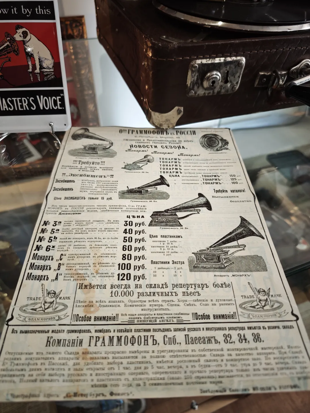A piece of paper with various turntable designs lies flat on a table, with Russian text printed on it. Above the paper is a suitcase, and other items are placed beside it. The background is an indoor environment.