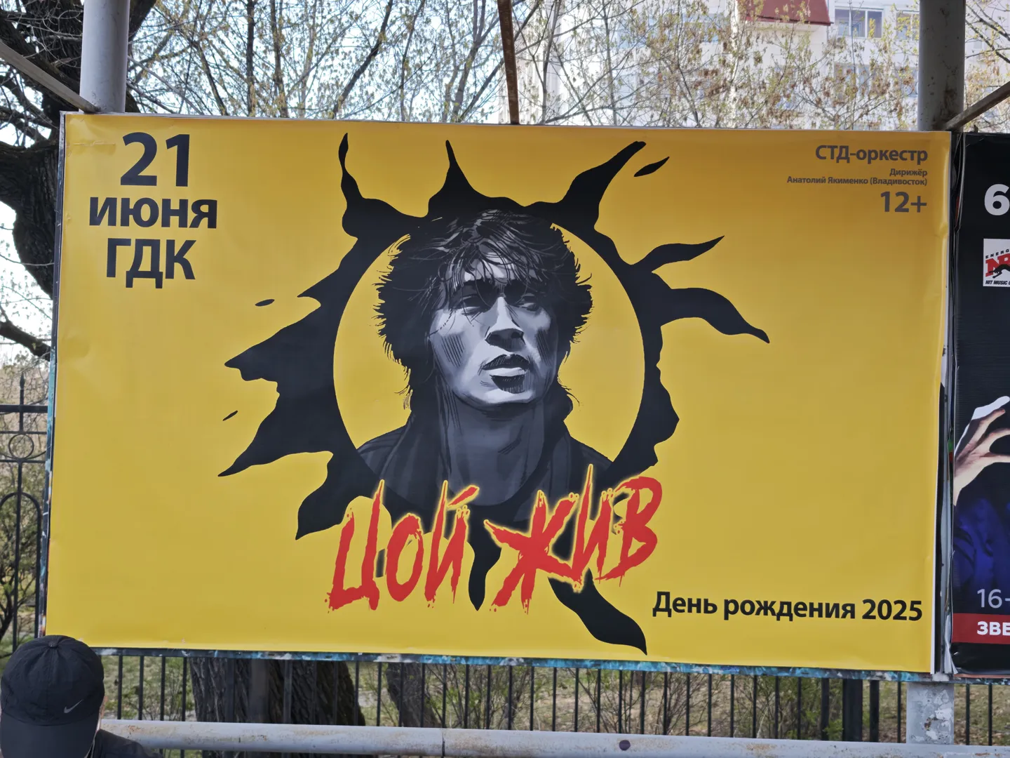 A poster with a yellow background shows a black silhouette, with the text “21 июня ГДК” next to it. Below the silhouette, red text reads “ЦОЙ ЖИВ,” and in the lower right corner, it says “День рождения 2025.”