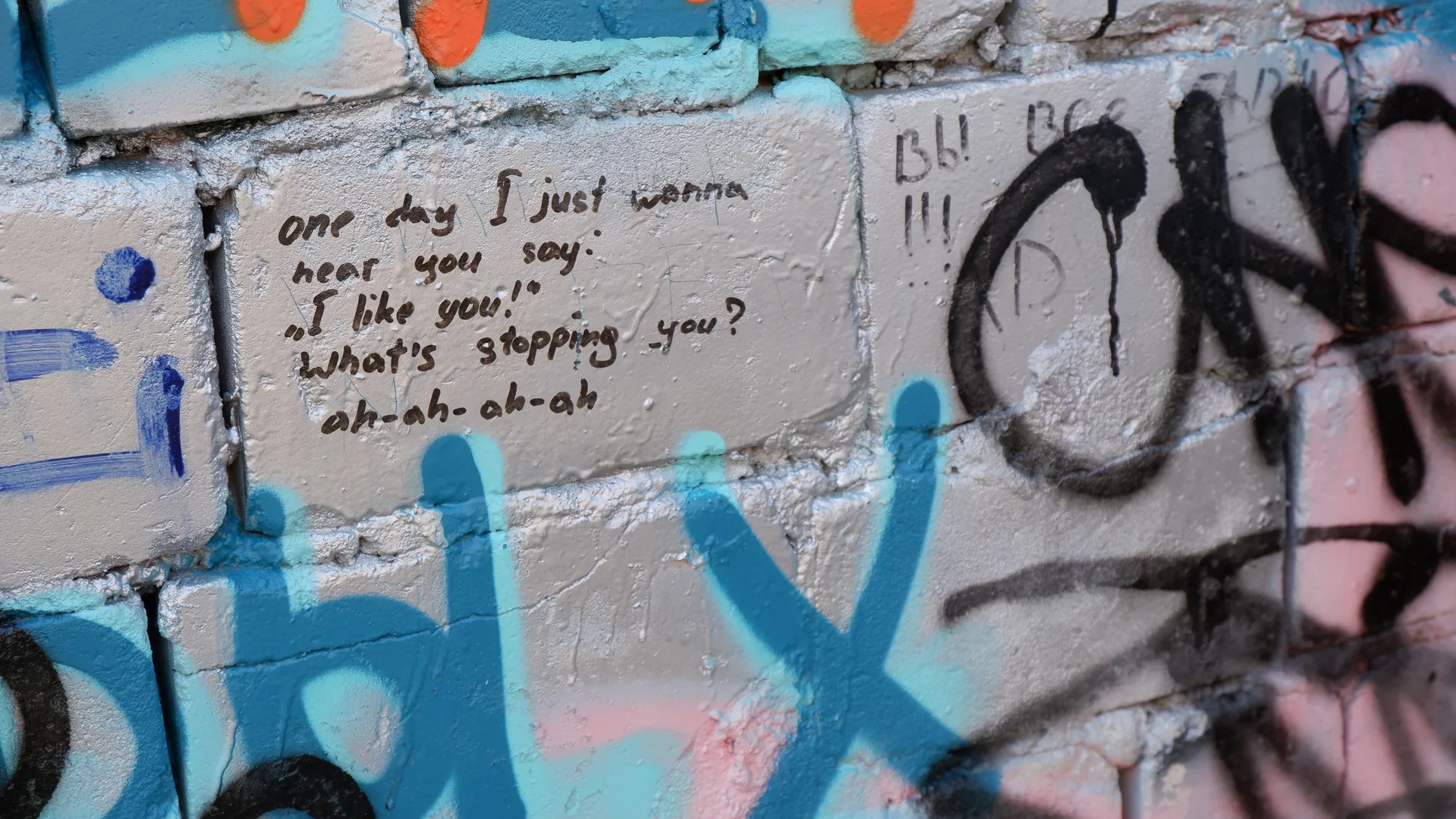 A segment of English graffiti on the wall, reading: “One day I just wanna hear you say: ‘I like you!’ What’s stopping you? ah-ah-ah-ah”. Colorful graffiti patterns surround the text.