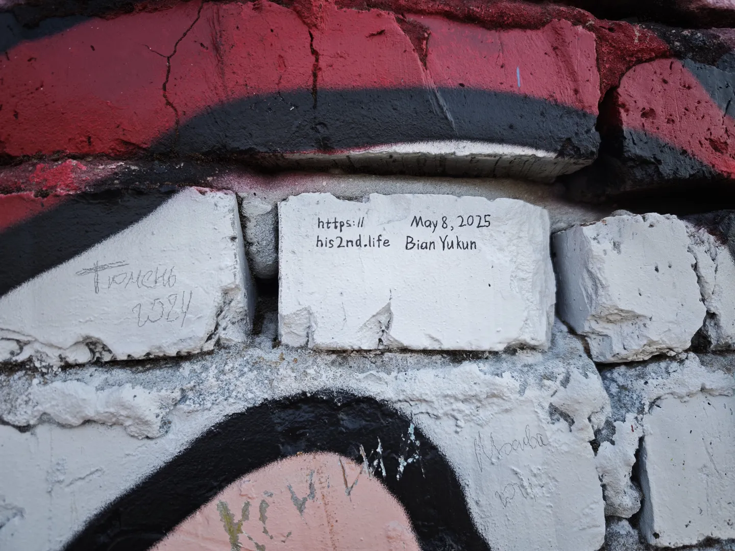 On a white brick wall, the same text “https://his2nd.life May 8, 2025 Bian Yukun” is engraved, surrounded by red and black graffiti patterns.