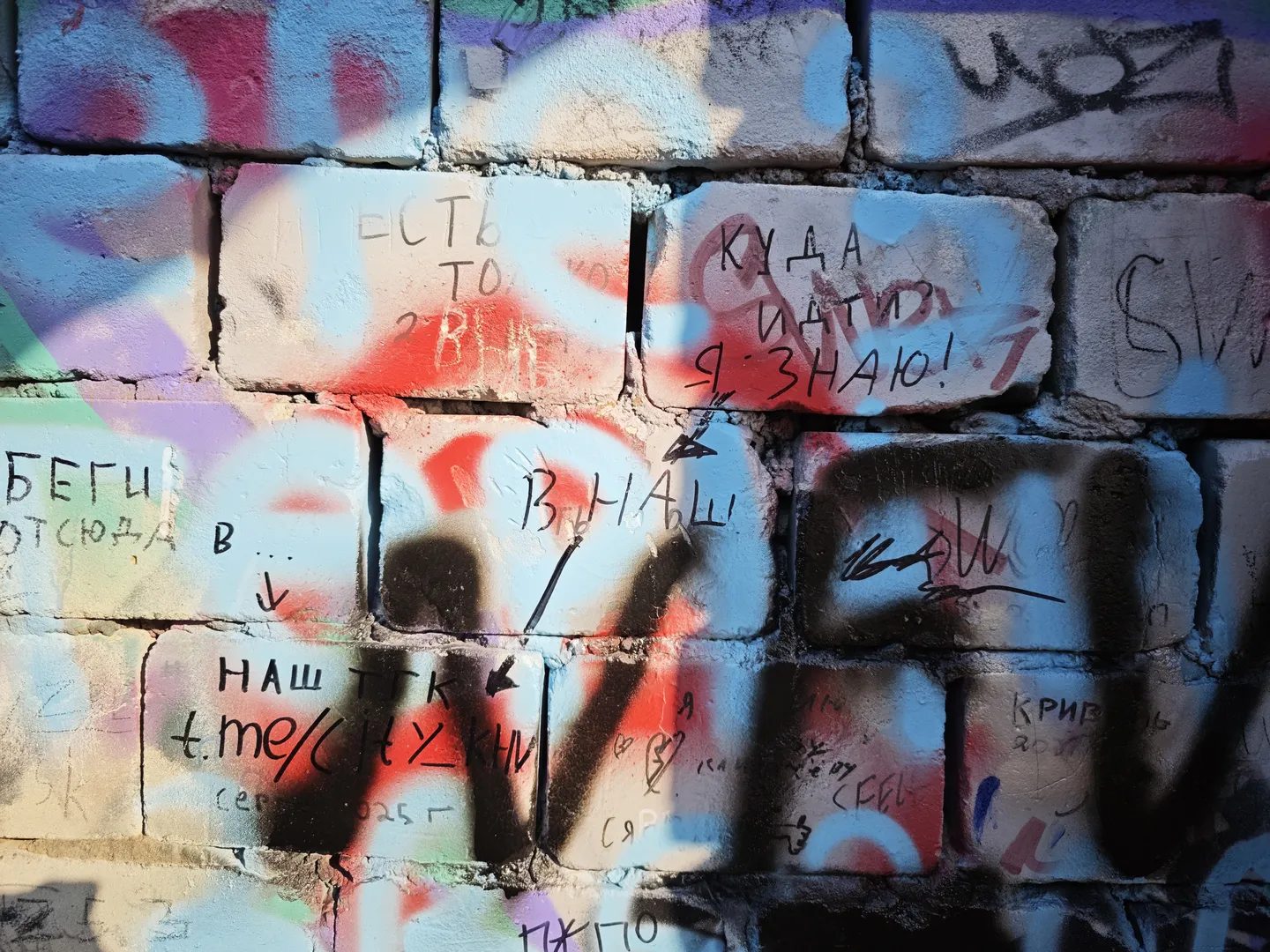 A brick wall covered with colorful graffiti, including Russian text and arrow symbols. The graffiti is vibrant and complex in design.
