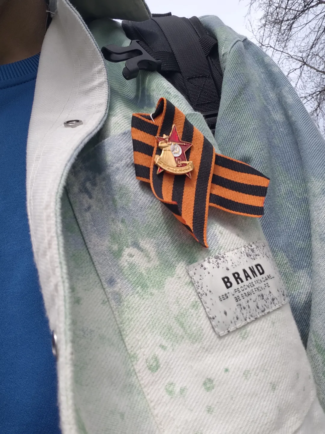 A light-colored jacket is adorned with an orange-black St. George ribbon and a red star medal. The inner lining of the jacket is blue, and there is a brand tag on the collar.