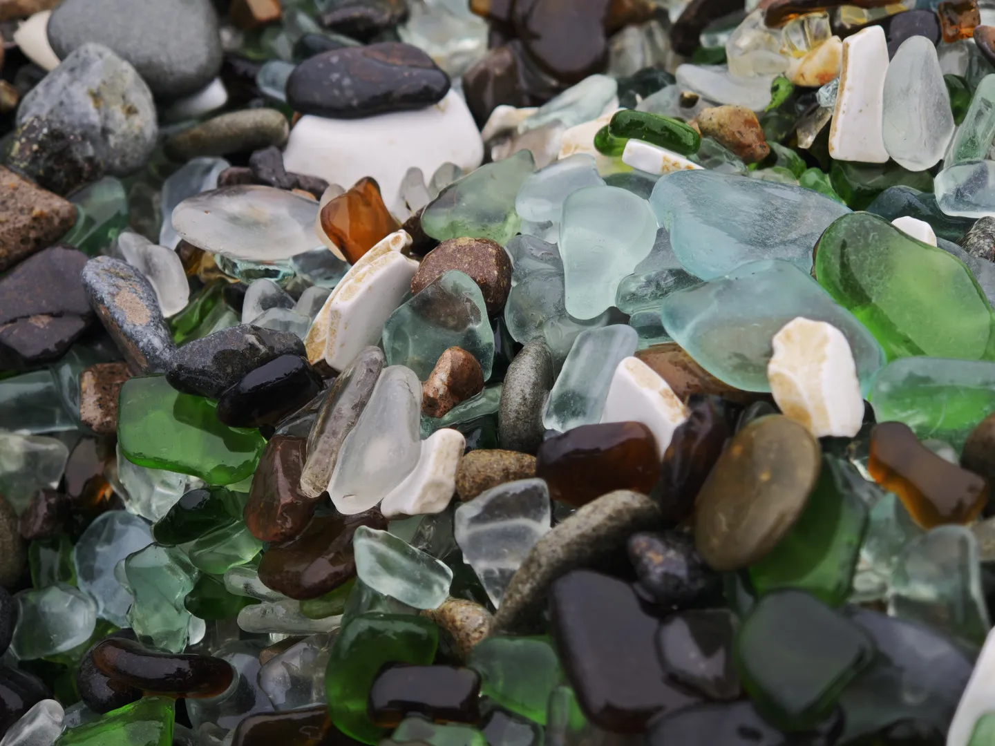 A pile of glass fragments and pebbles in various colors, including green, blue, brown, and clear. The fragments are of different shapes and sizes, creating a dense appearance.
