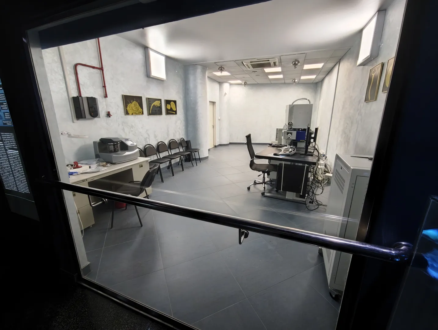 Inside a laboratory, there are desks, chairs, and professional equipment. Several decorative paintings hang on the walls, and the floor is covered with gray tiles. The room is neat and orderly, with light and bright illumination.