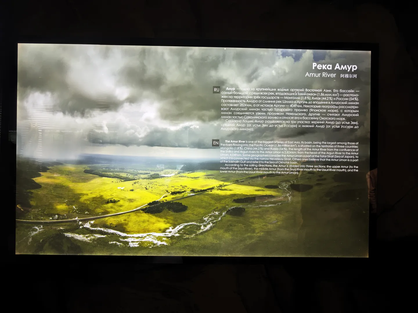 Screen displays information about “Amur River”, describing its geographical location and watershed characteristics. The Amur River is one of the largest rivers in East Asia, flowing through Mongolia, China, and Russia. The picture shows the river flowing through a vast green plain.