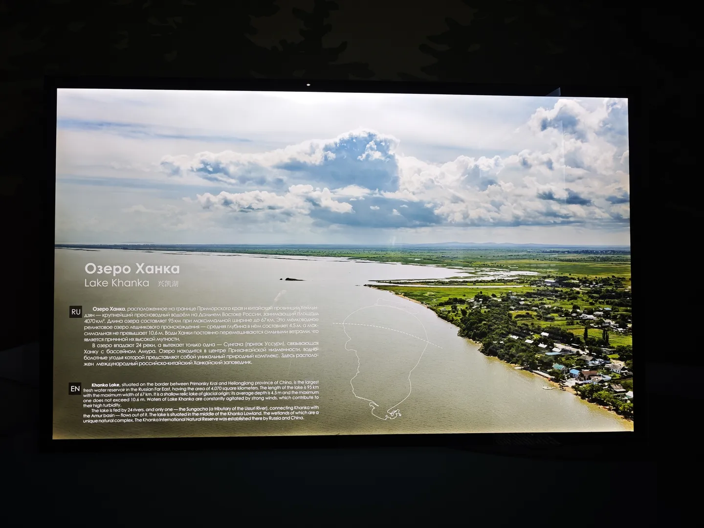 The screen displays information about “Lake Khanka”, describing its location on the China-Russia border. The lake covers an area of 4,070 square kilometers, with a length of 95 km and a maximum width of 67 km. The image shows the green landscape surrounding the lake.