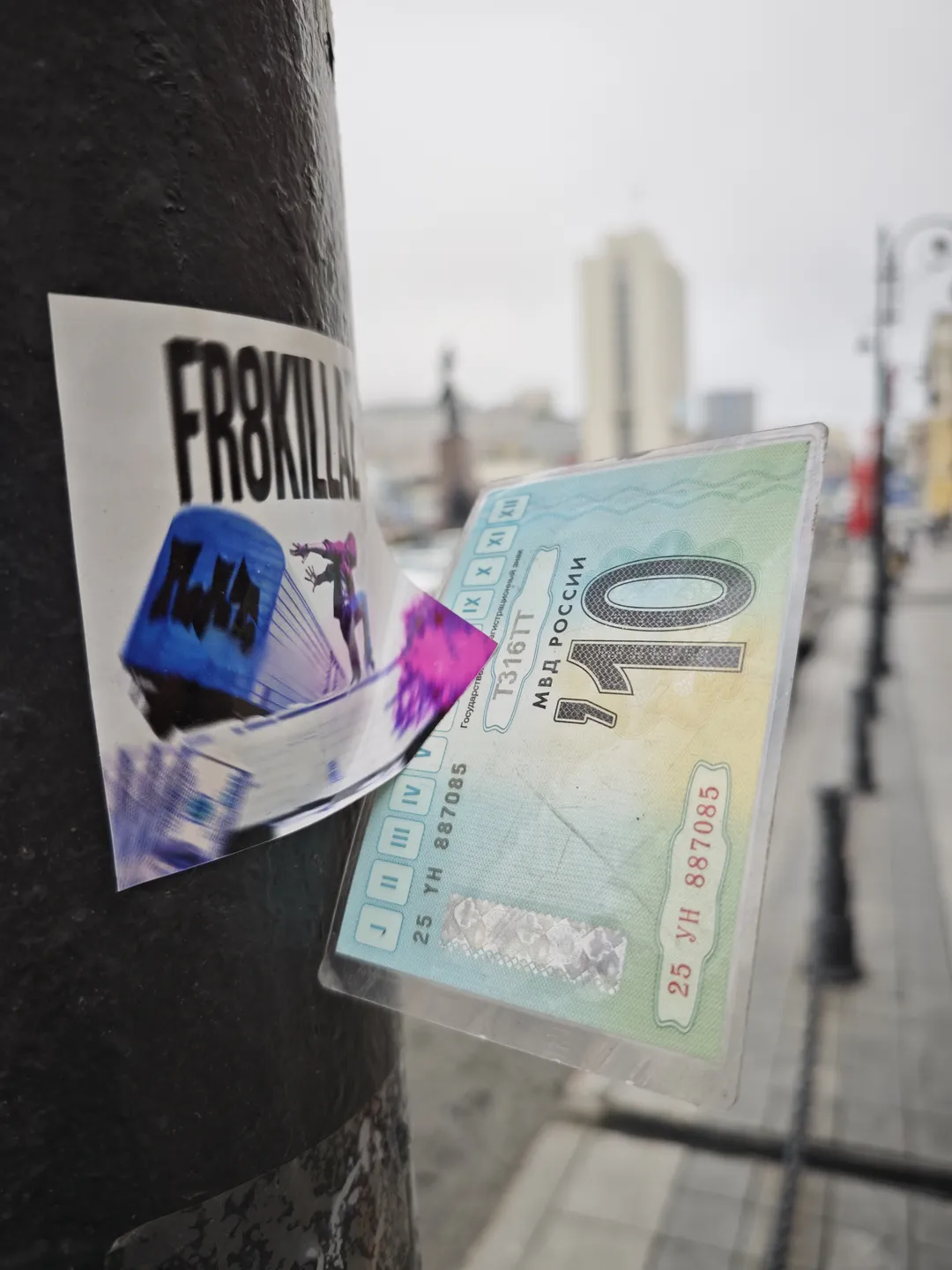 A sticker is affixed to a pillar, bearing the words “FR8KILLA” alongside a transparent plastic bag containing a card with the number “110” and Russian text.