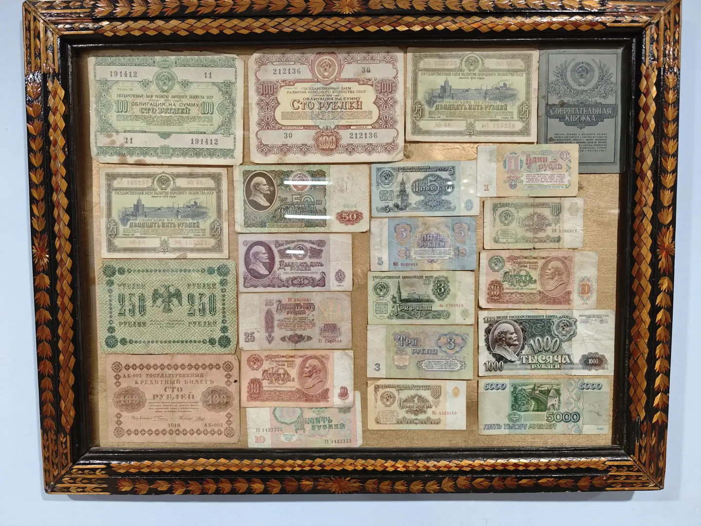 一个装饰性画框内陈列着多张不同年代的苏联纸币，面额从1到5000卢布不等，纸币颜色多样，部分印有人物肖像和建筑图案。