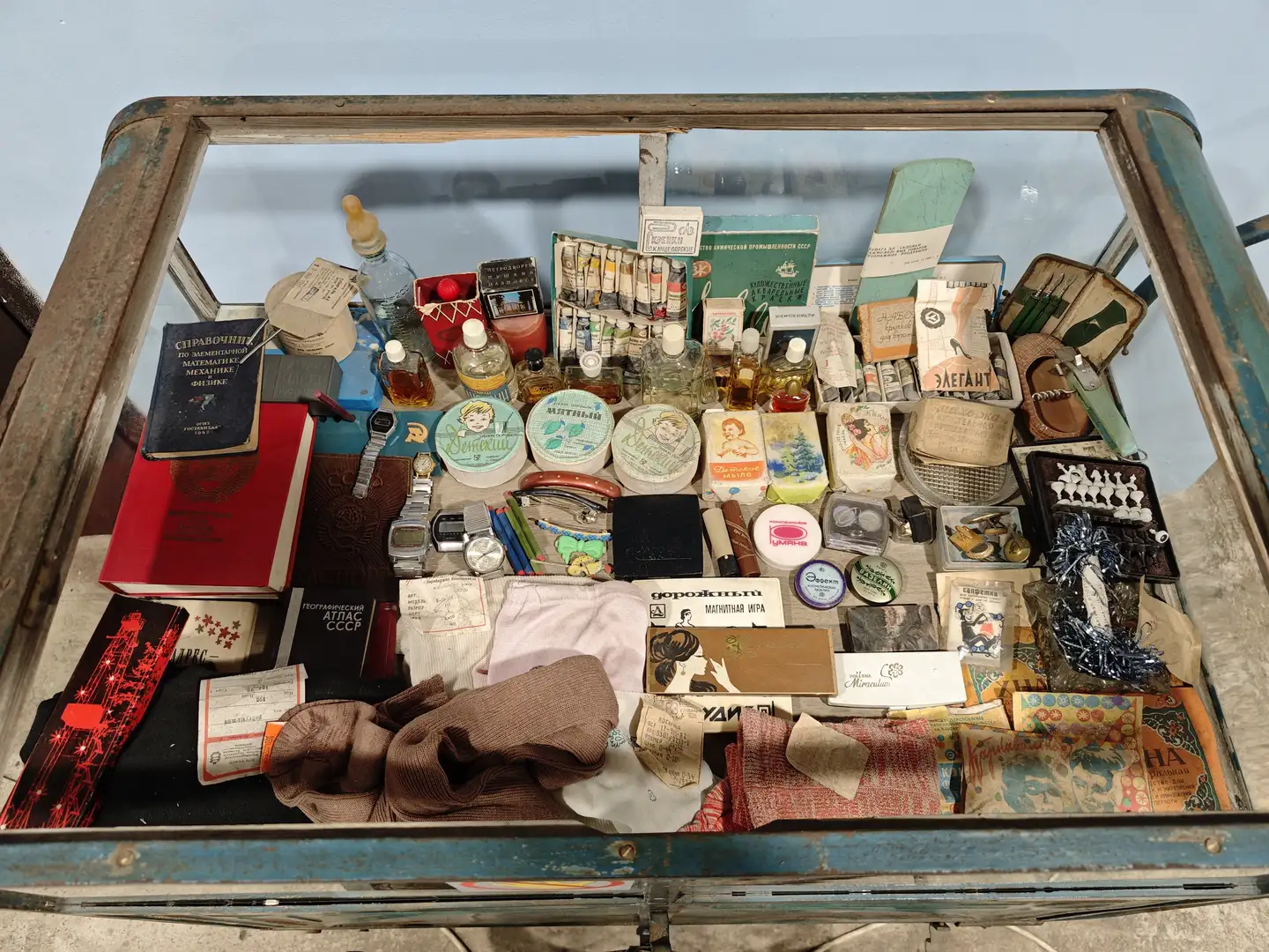 一个旧式玻璃箱内展示着大量怀旧物品，包括书籍、手表、化妆品、香皂、衣物、工具和小饰品，物品排列密集，具有浓厚的时代特征。