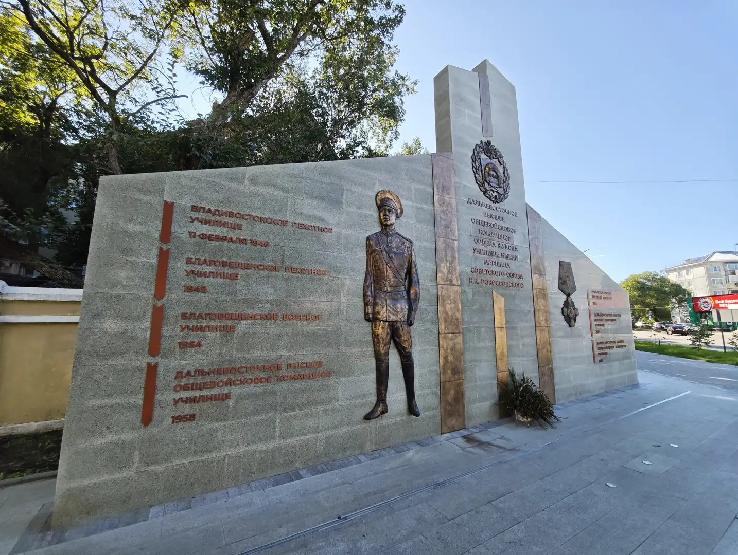 灰色石墙上镶嵌着一位军人的浮雕，旁边刻有历史信息和勋章图案，记录了军事院校的发展历程。