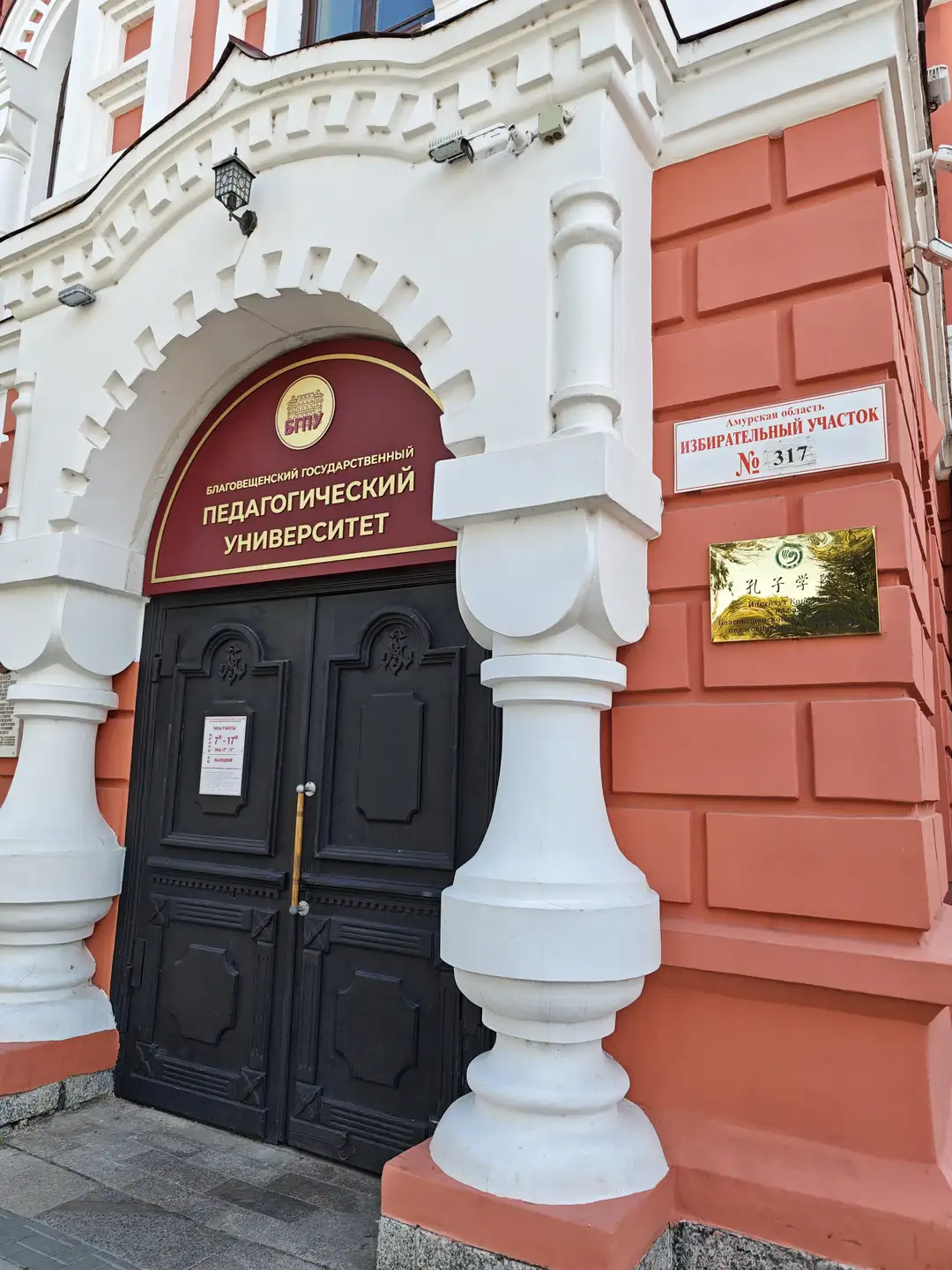 红白相间的建筑入口上方悬挂着“Благовещенский государственный педагогический университет”的标牌，门旁有中文“孔子学院”铭牌。
