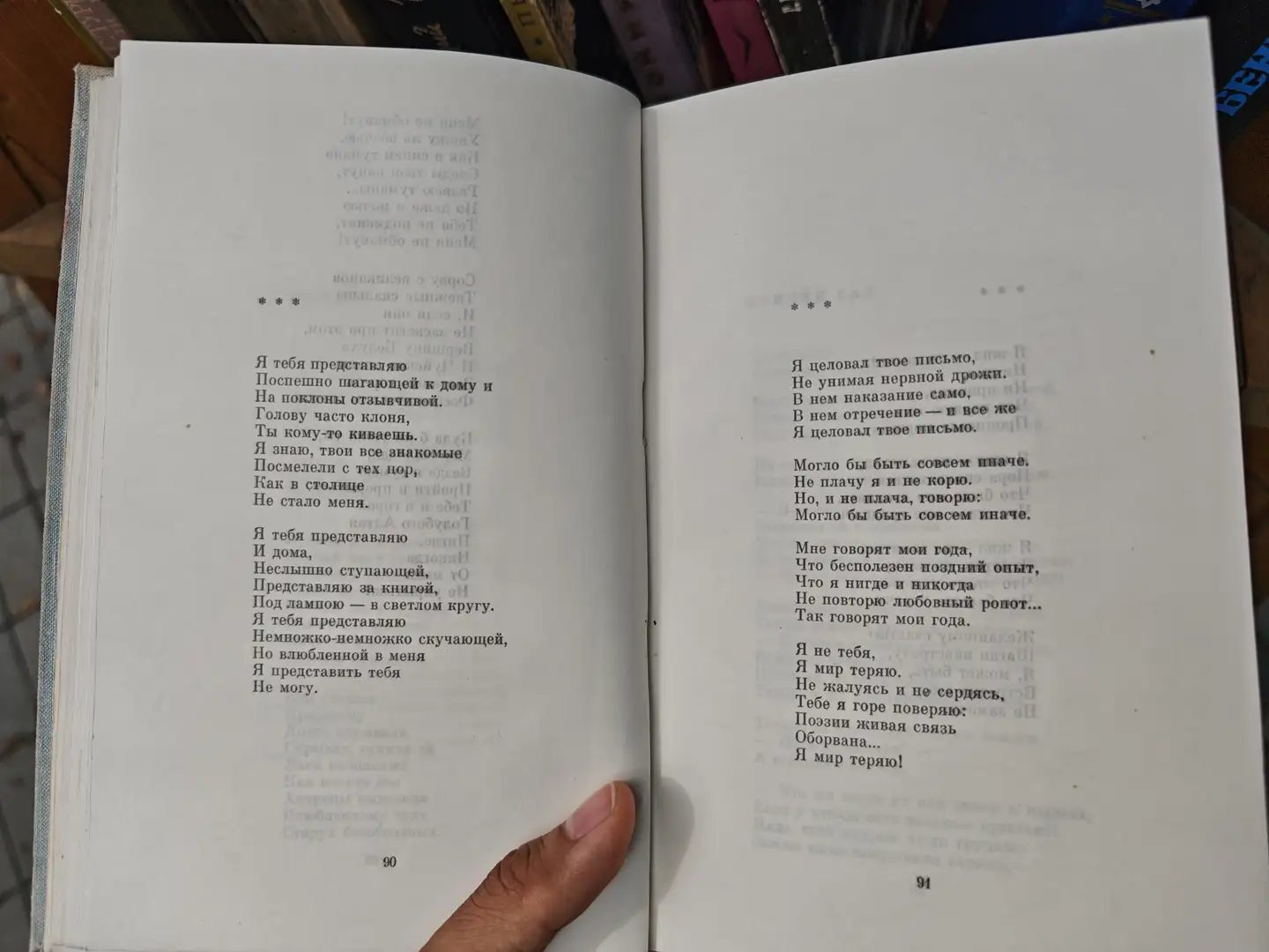 书页上印有俄文诗歌，文字排列整齐，页面边缘有轻微折痕。左侧页面底部标有页码90，右侧为94，手指轻按在书页中间。