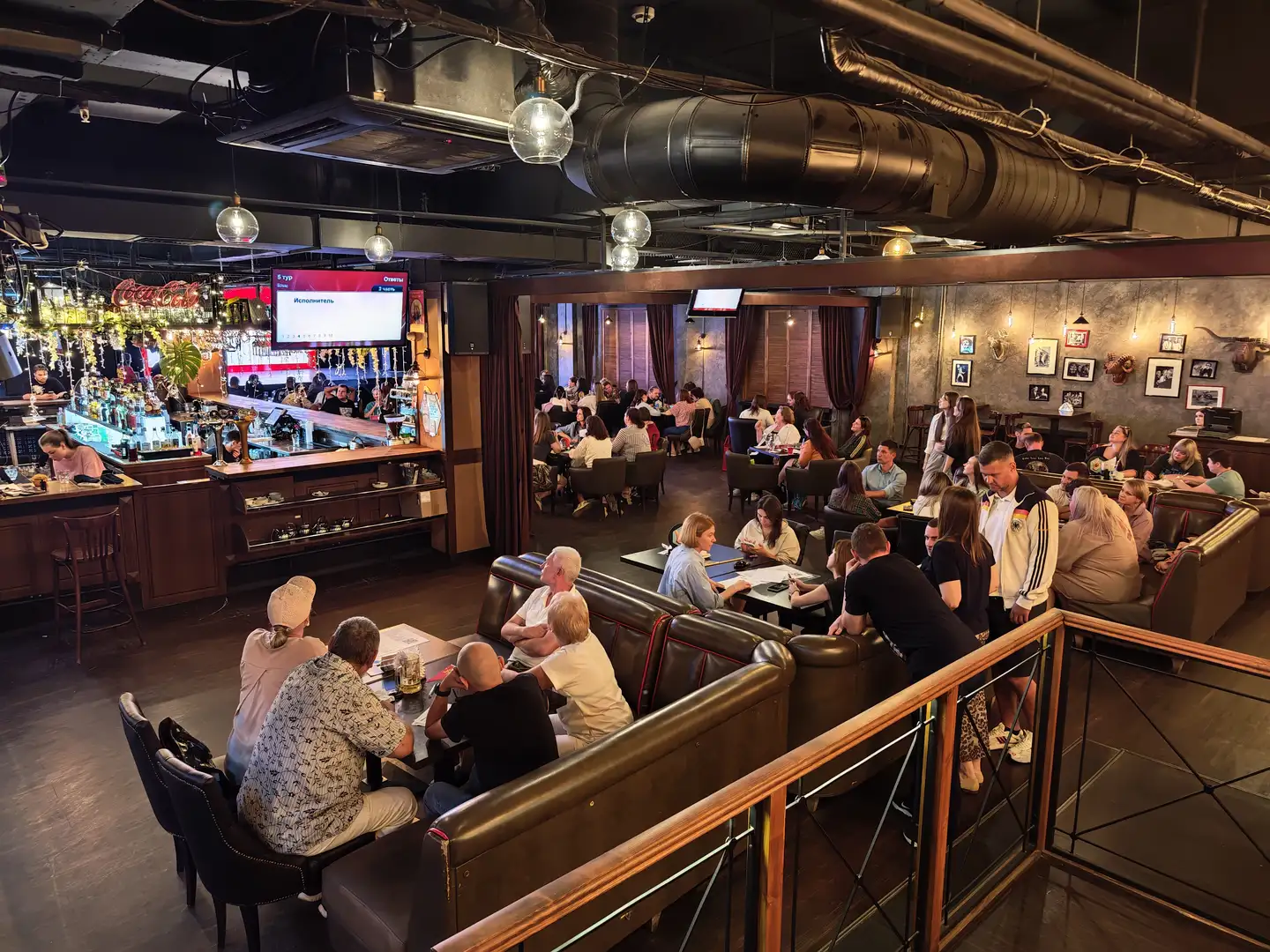 餐厅内坐满了客人，他们围坐在桌旁或靠在沙发卡座上，天花板上裸露的管道和吊灯营造出工业风格氛围