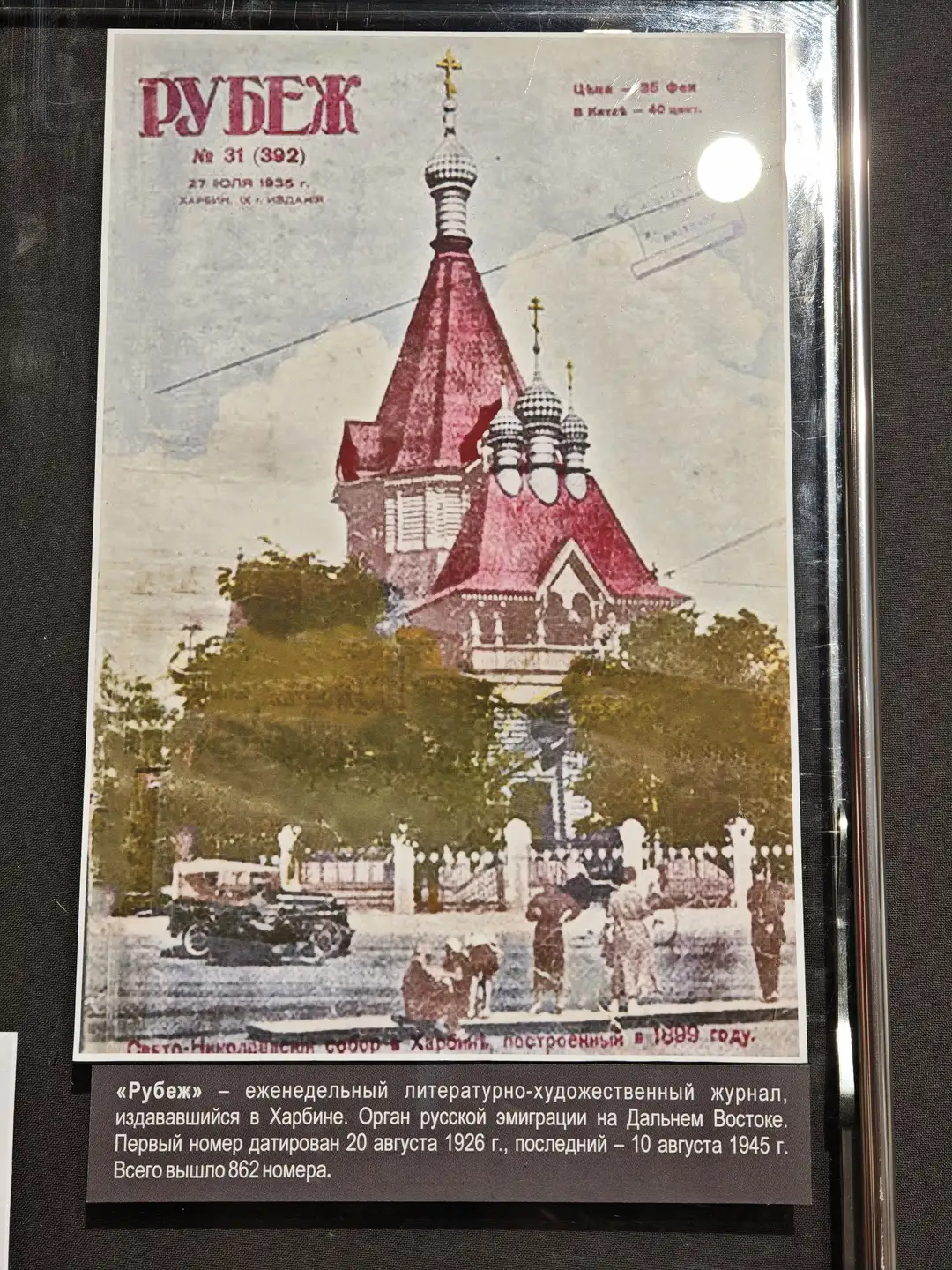 一本名为《РУБЕЖ》的杂志封面展示了一座红色屋顶的教堂，周围有树木和行人，前景中有汽车和马车。封面上方标注了日期“27 июля 1935 г.”和地点“Харбин”。下方的文字说明这是一本在哈尔滨出版的文学艺术期刊，共发行862期。