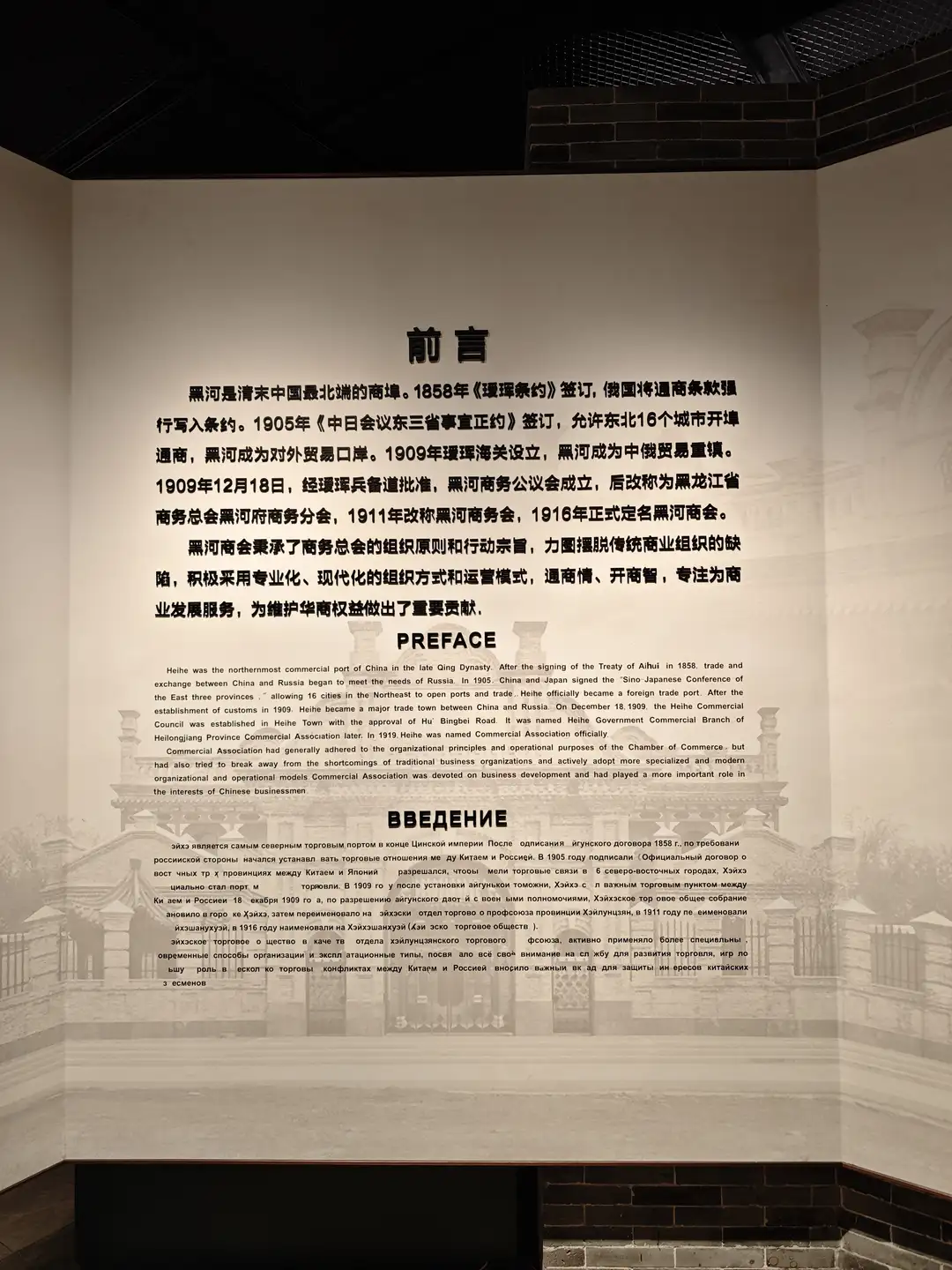 一面墙上的展板，标题为“前言”，内容介绍黑河的历史背景，包括其作为商埠的发展历程和中俄贸易关系。展板上有中文、英文和俄文三种语言的文字说明。背景是模糊的建筑图像。