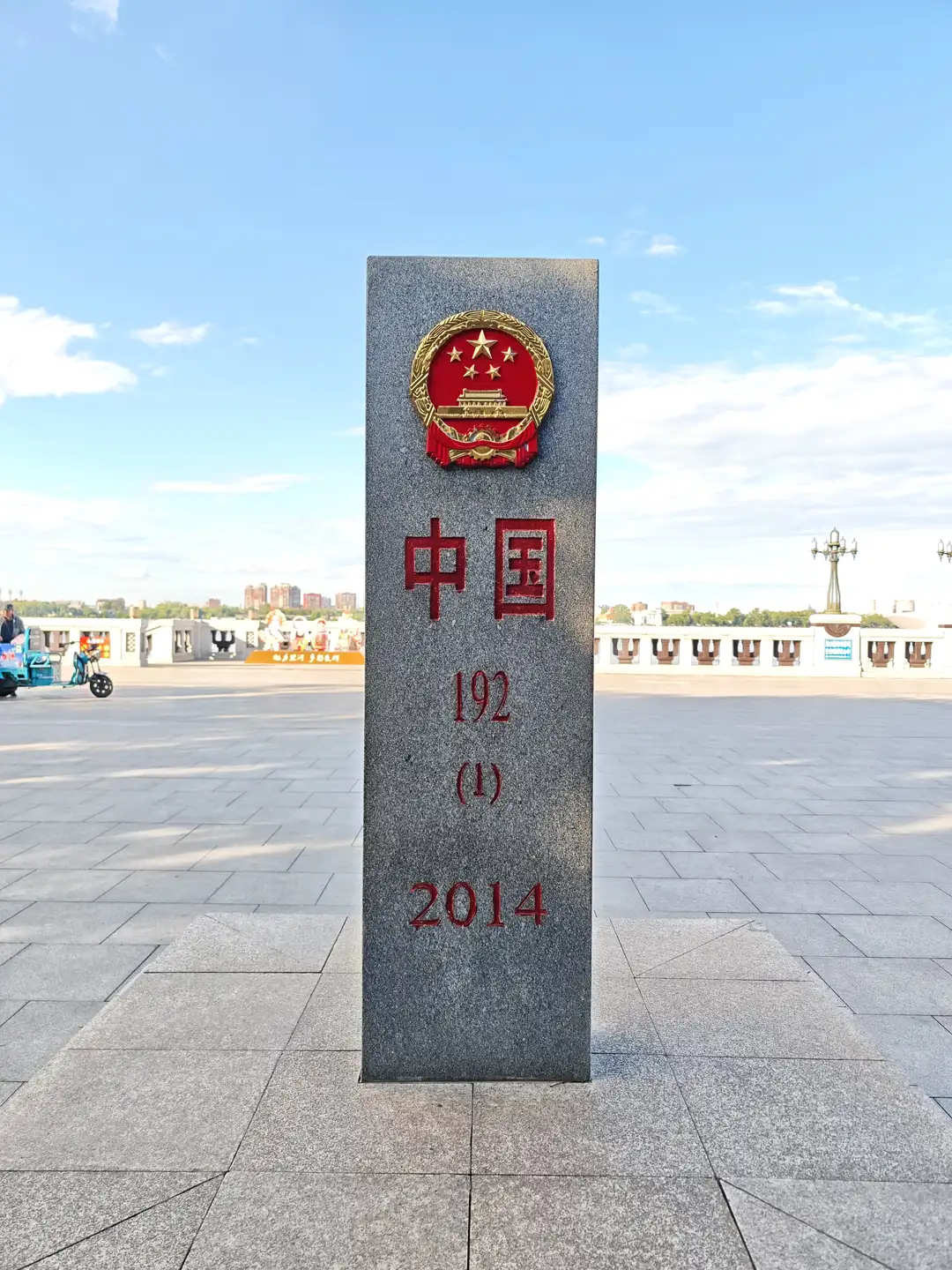 一块高大的灰色石碑矗立在开阔的广场上，顶部有中华人民共和国国徽，下方刻有“中国 192 (1) 2014”的红色文字