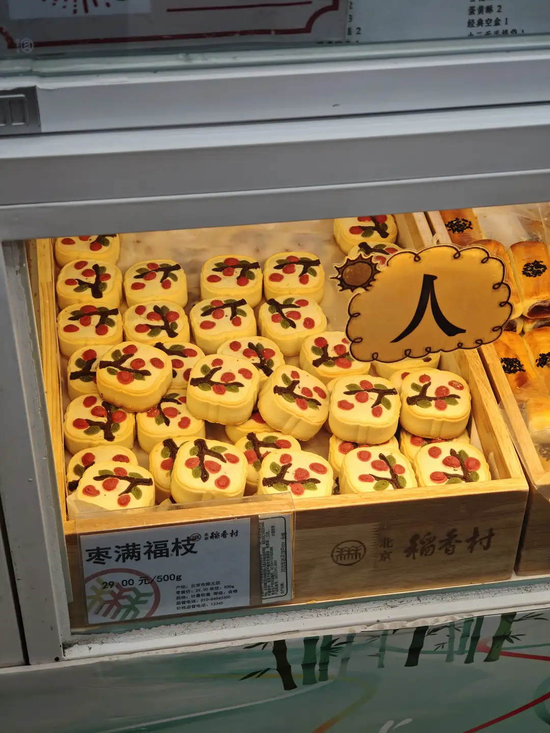 展示柜里陈列着许多黄色糕点，上面装饰有红色果实图案。糕点整齐排列，标签上写着“枣满福枝”。价格为29.00元/500g。