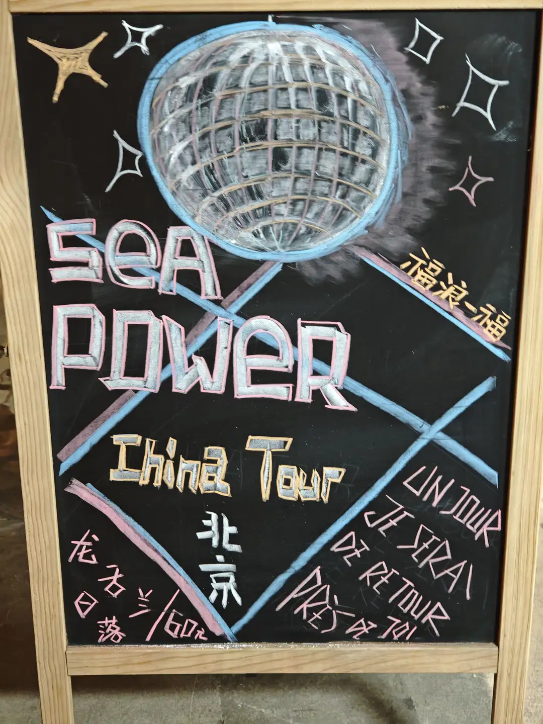 黑板上画着一个迪斯科球，上面写着“SEA POWER China Tour”以及一些中文和法文文字。黑板周围装饰有星星图案，整体设计色彩鲜艳。