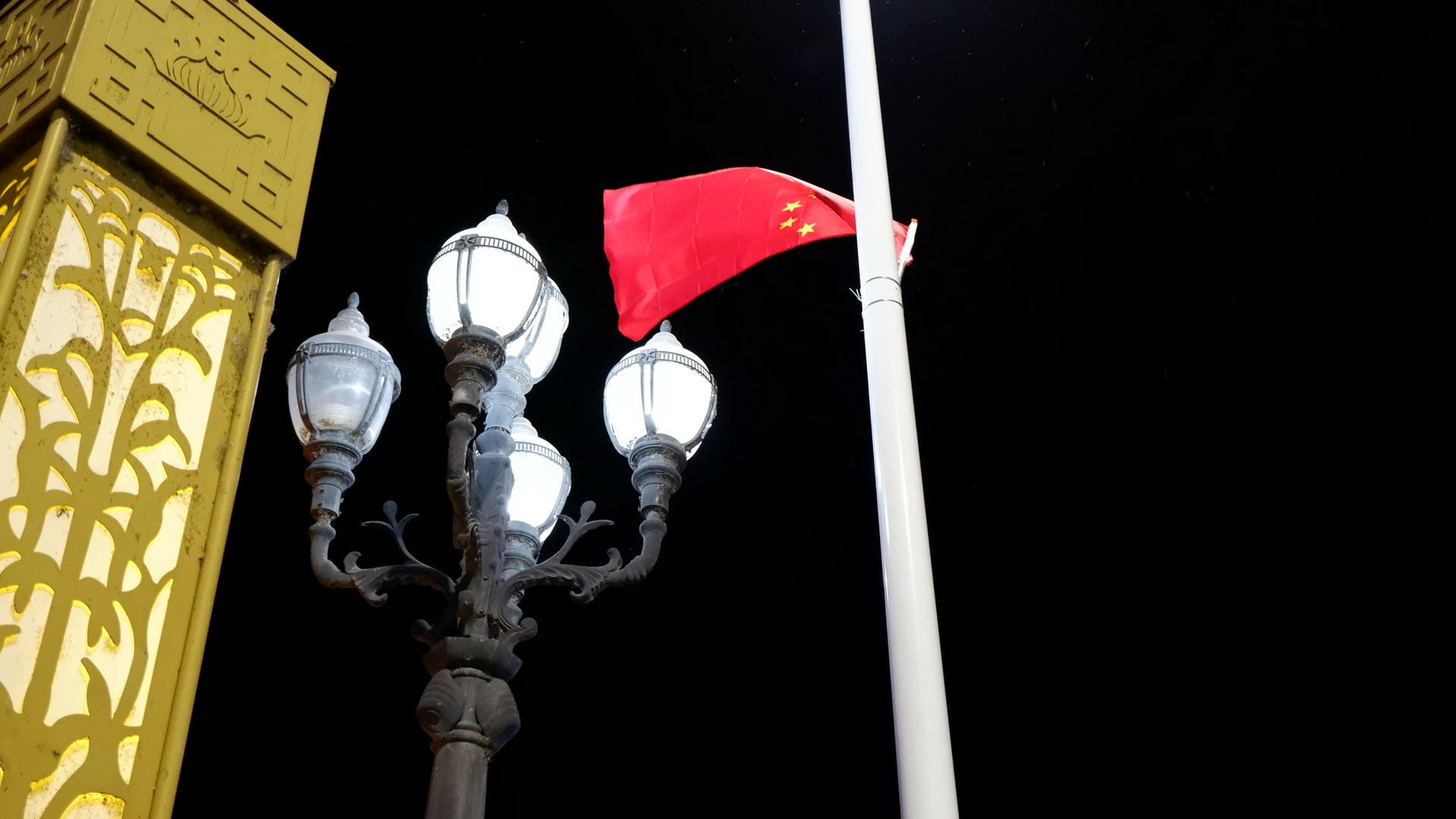 A Chinese flag fluttering beside a streetlight at night.