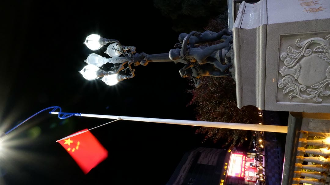 A Chinese flag fluttering in the night, next to a decorative streetlight.