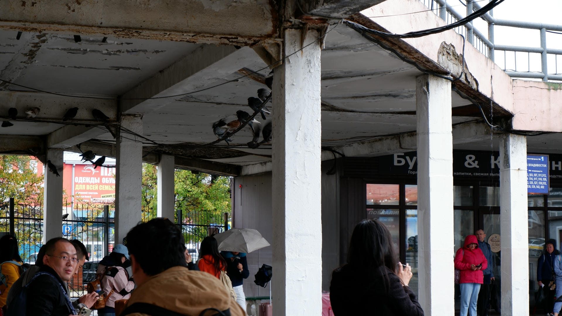 Several people sheltering from rain under an awning, with shop signs visible in the background.