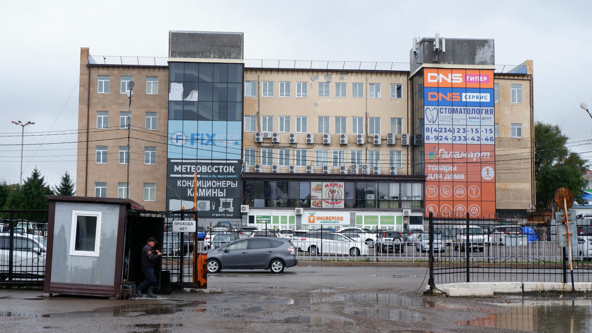 A group of people gathered in front of a building, with birds perched on overhead beams.