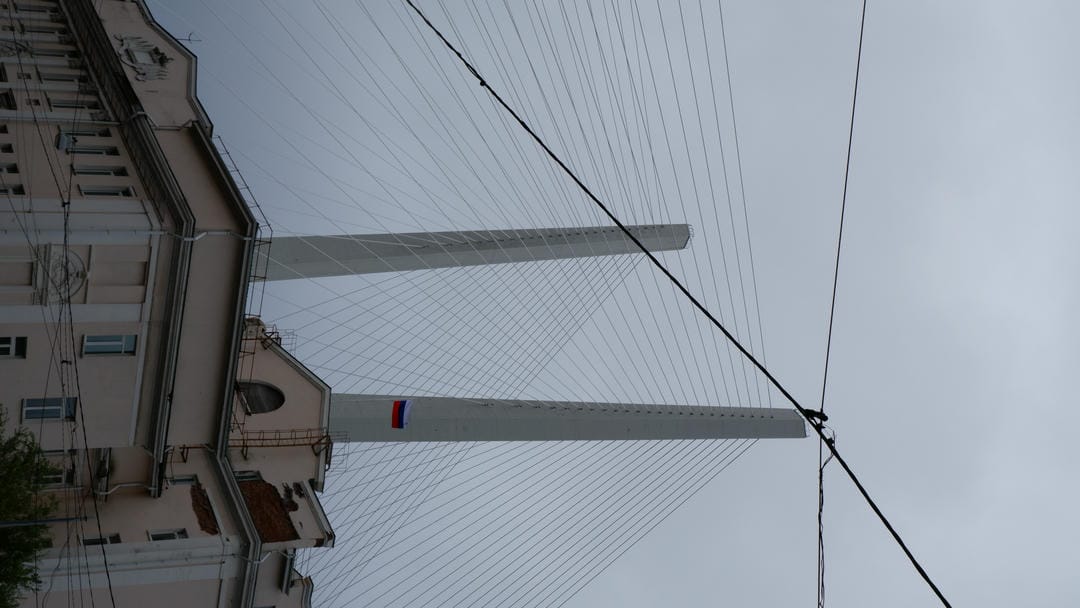 Two towering bridge pylons piercing the clouds, with Russian flags hanging from the bridge.