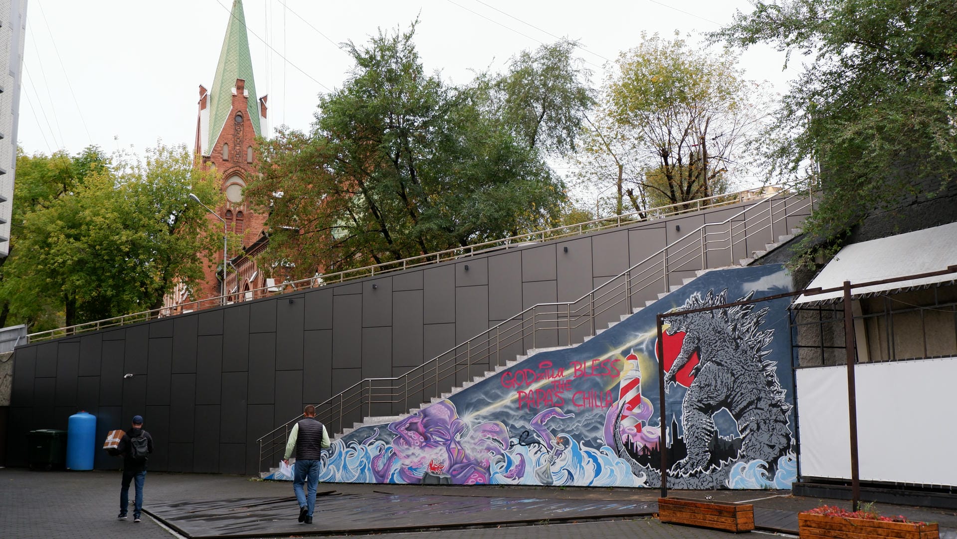 Church steps featuring a Godzilla-themed mural, with two pedestrians passing by.
