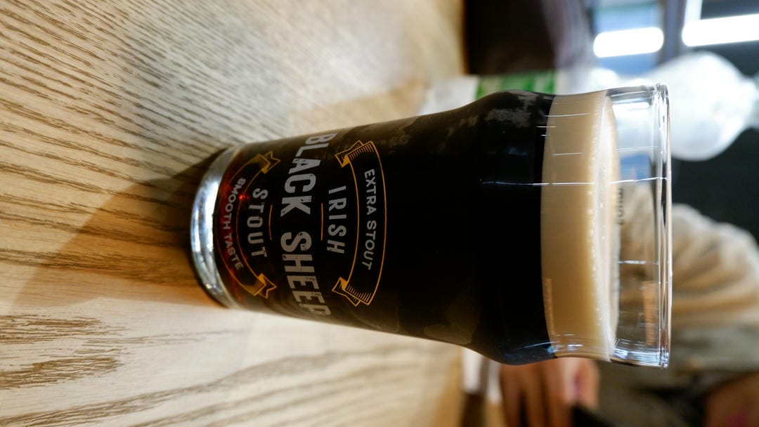 A glass of “Irish Black Sheep Stout” beer placed on a wooden table.
