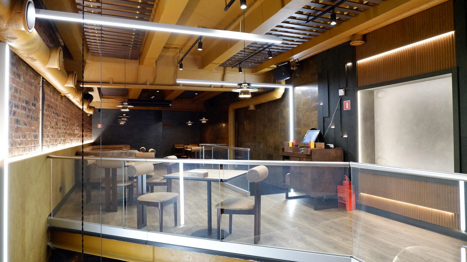 Cafe interior with glass-partitioned seating area and exposed pipes/lighting fixtures on ceiling.