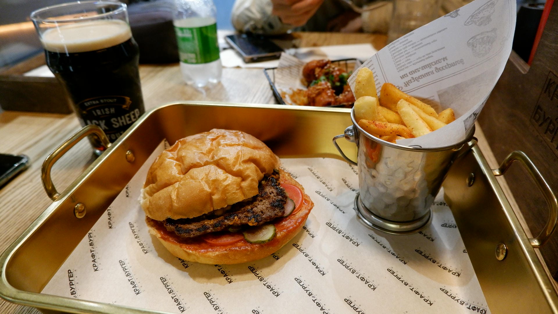 A tray holding a burger, bucket of fries, and a dark beer.
