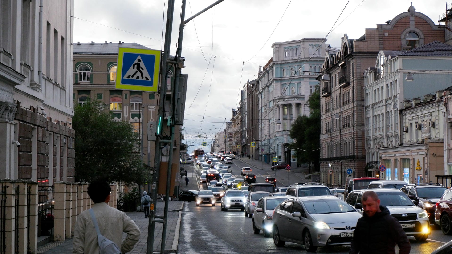 Busy urban street flanked by European-style buildings, filled with traffic and crossing pedestrians.