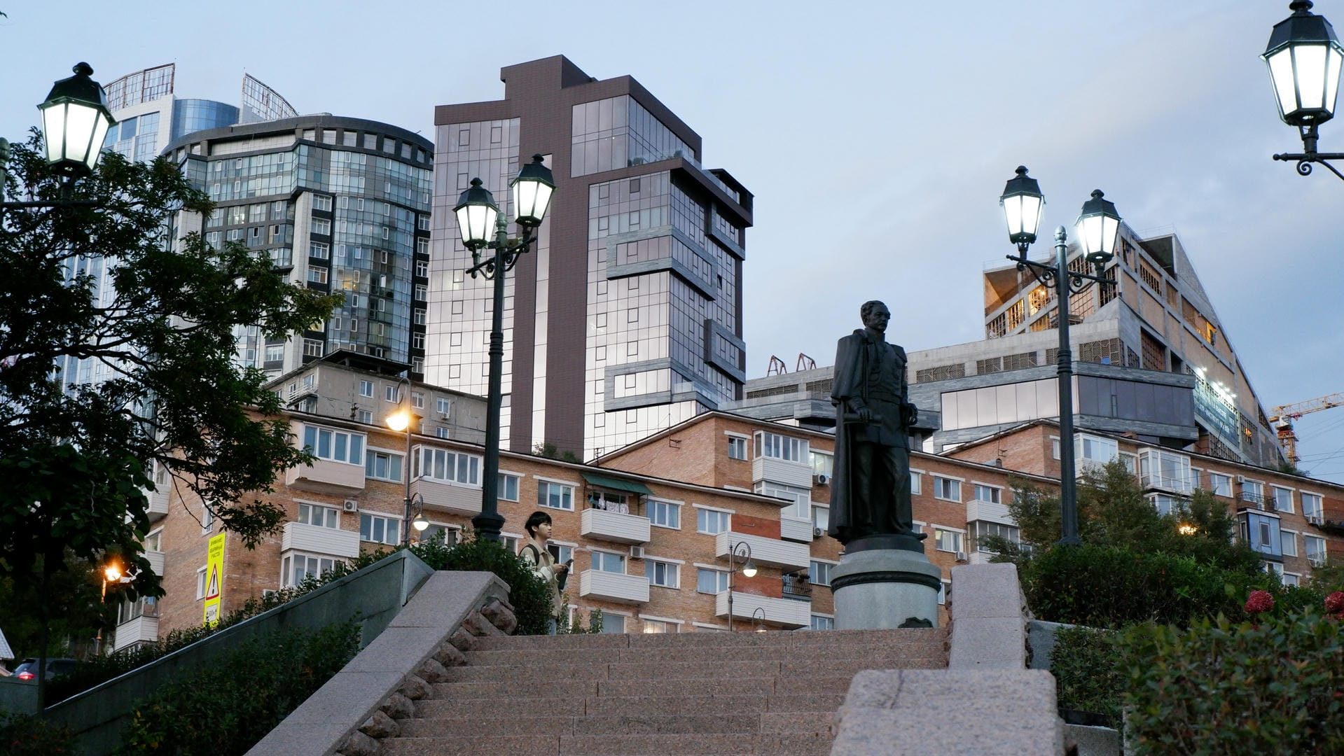 Night cityscape featuring a statue in foreground and modern skyscrapers in background.