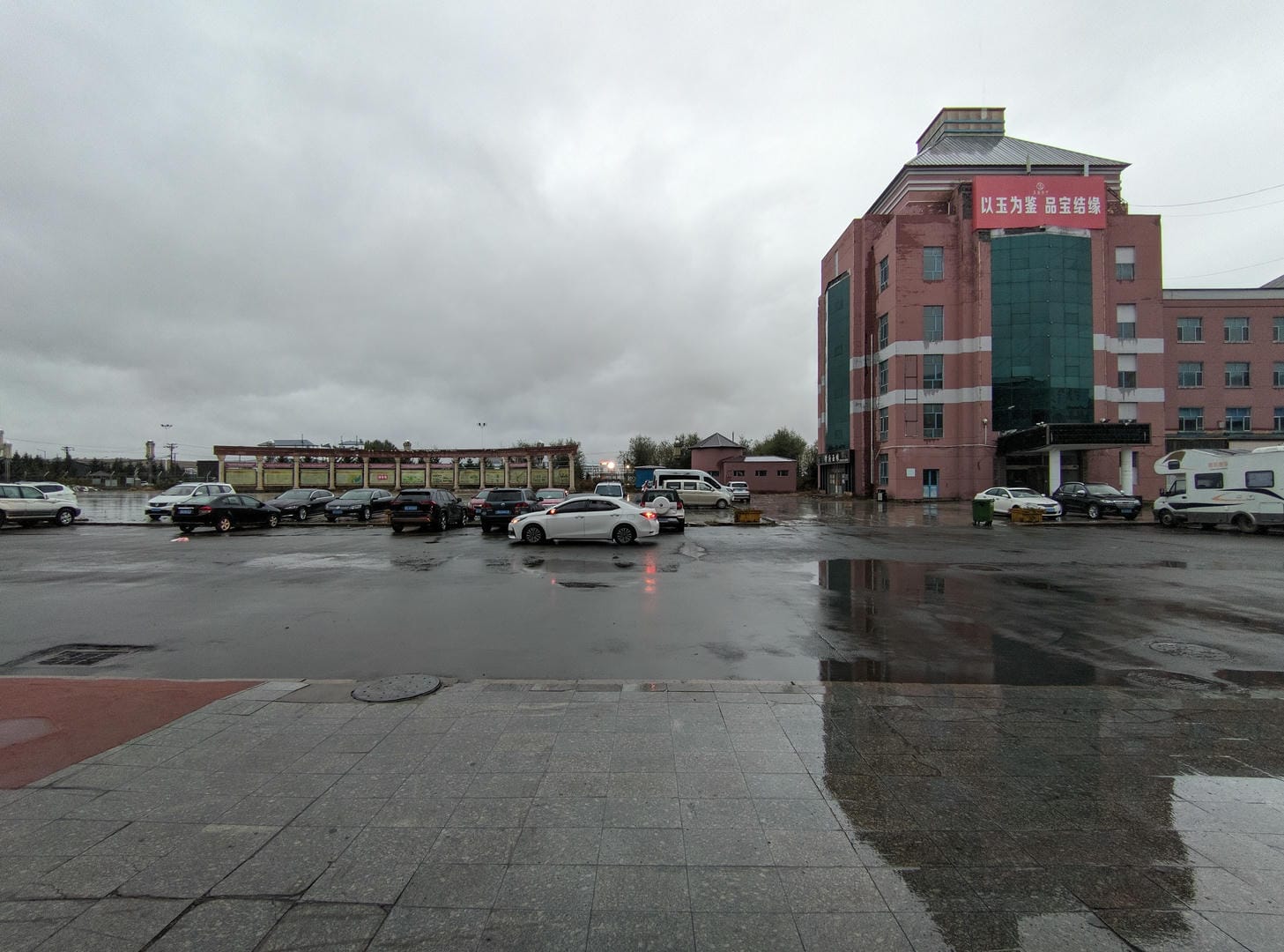 A wet square with parked cars and a pink building on the right.