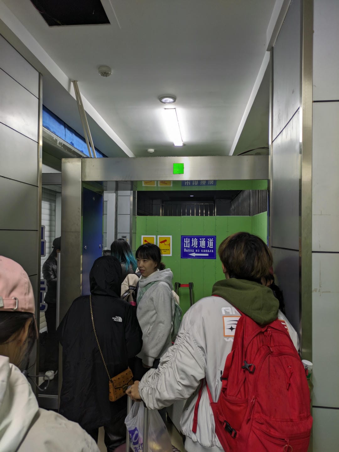 People waiting in a passageway with green “Exit Channel” sign at the end.