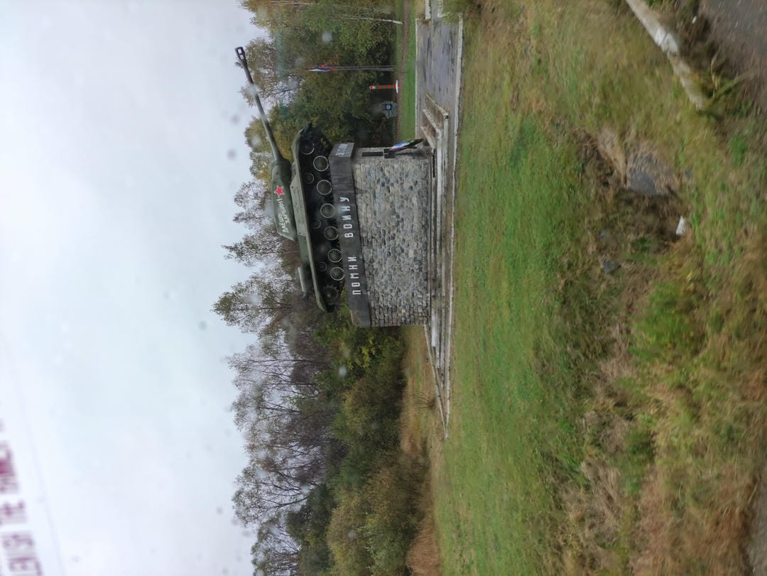 Tank monument with red star emblem, surrounded by grass and trees.