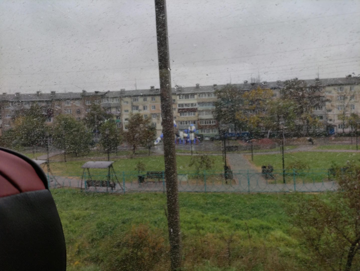 Car window view of residential area with distant buildings and playground equipment.