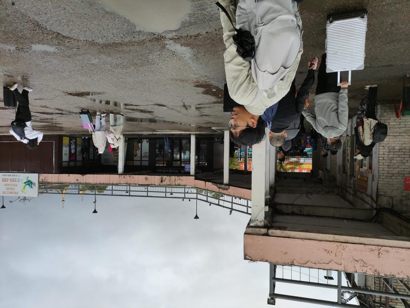 People walking outside station with luggage, buildings in background.