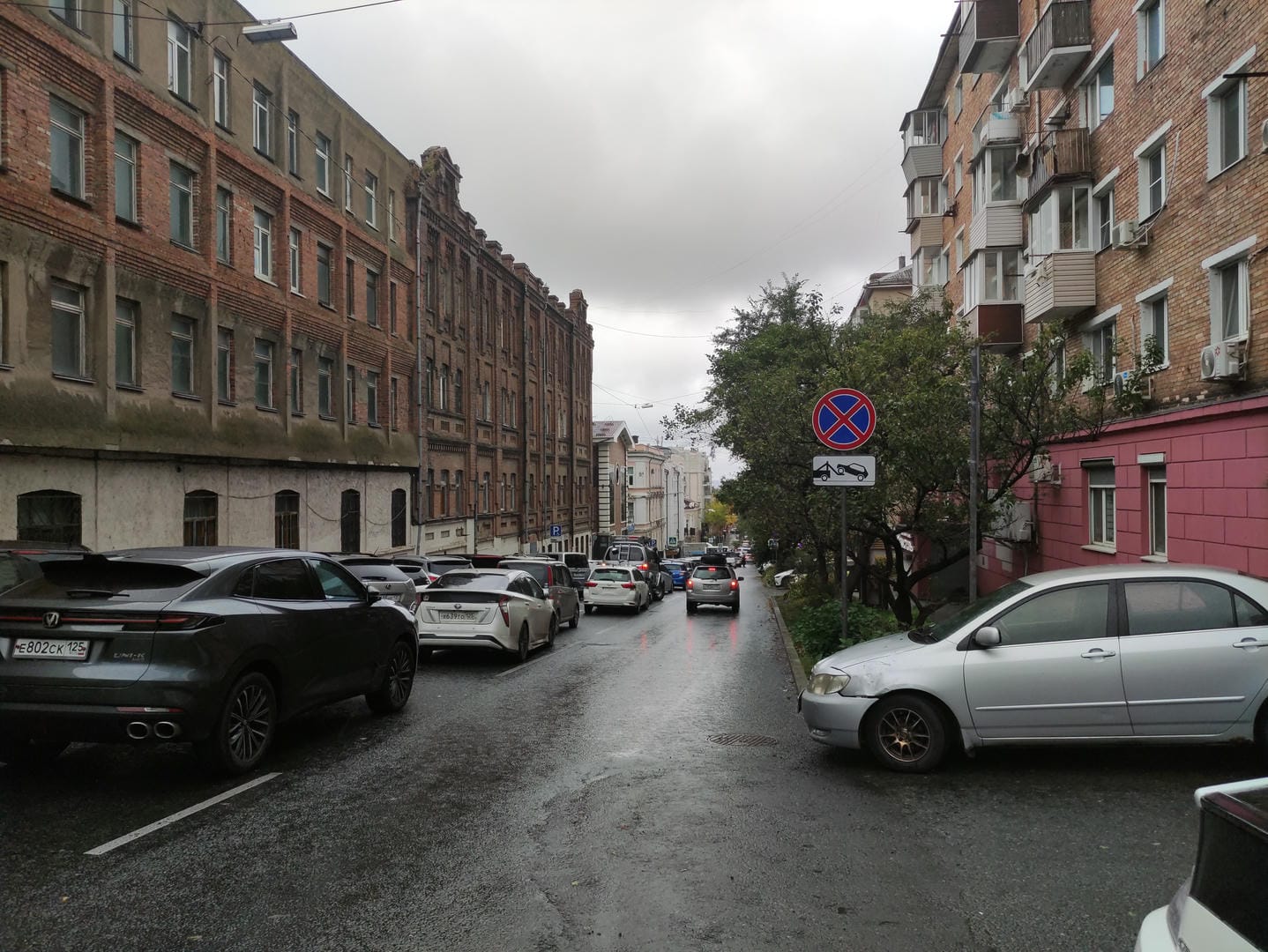 Street lined with cars, older buildings on left and colorful ones on right.