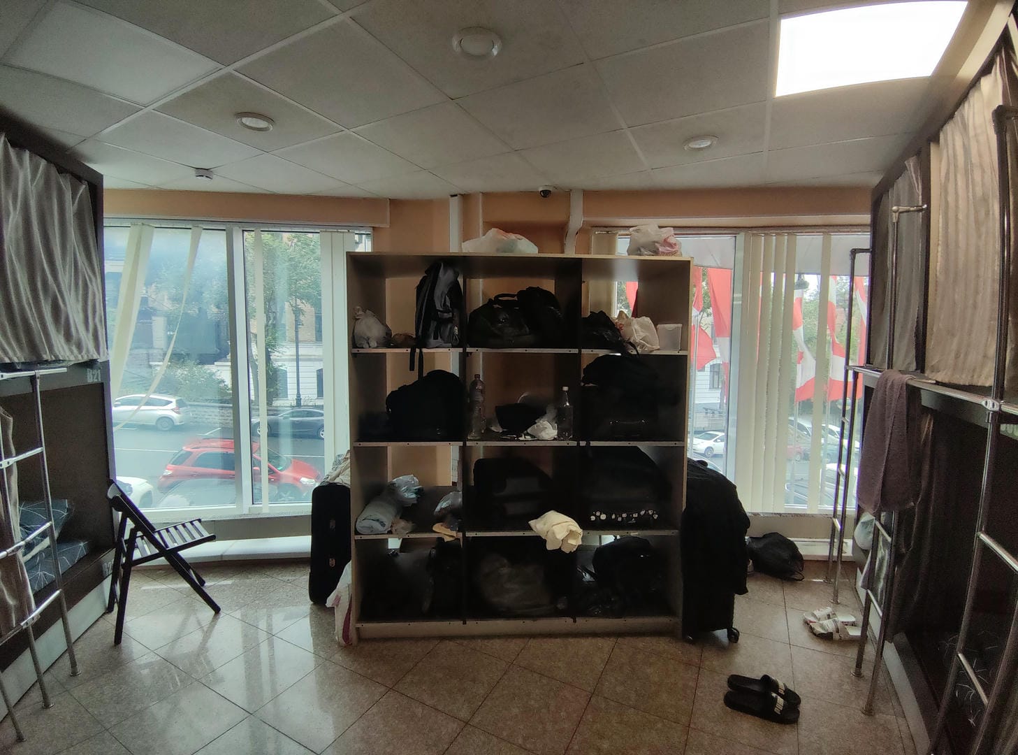 Room with large bookshelf holding black bags, chairs by window.