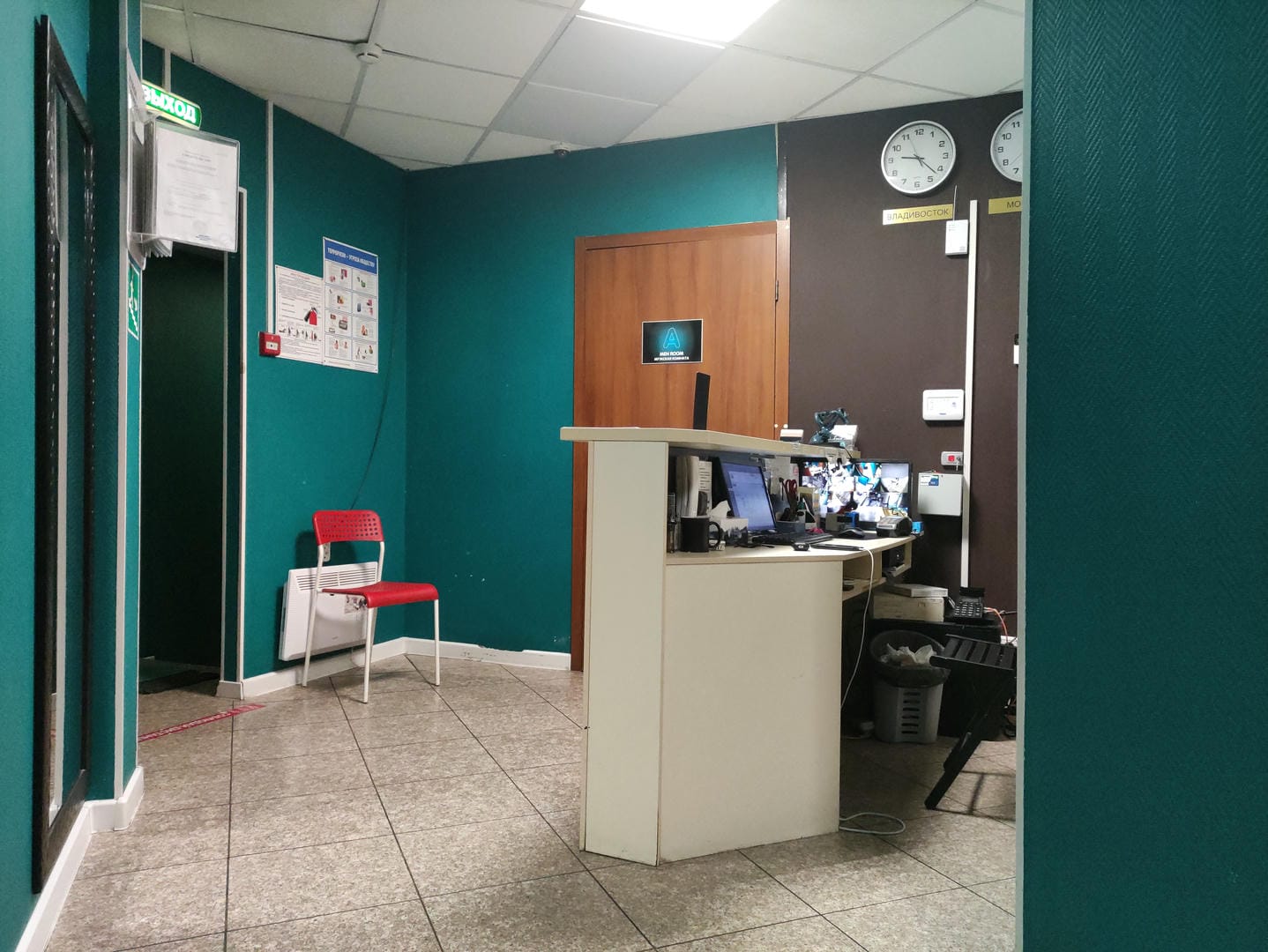 Reception area with green walls, white counter with computer, wall clock.
