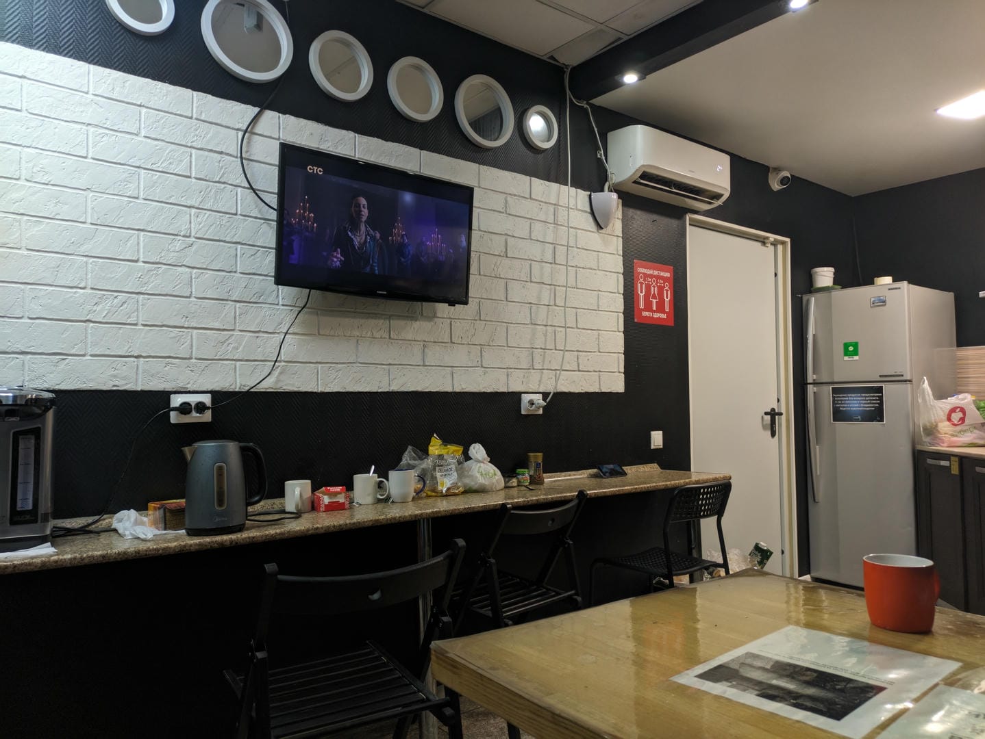 Kitchen area with TV on wall, kettle/cups on counter, refrigerator at right.